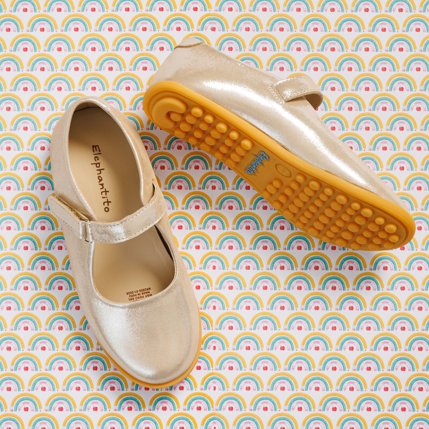 Elephantito - Shiny pale pink Mary Jane shoes with adjustable strap and textured yellow rubber soles on rainbow-patterned background.