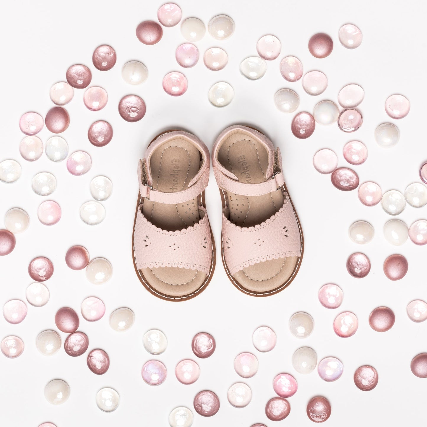 Pink toddler sandals with scalloped edges and ankle straps surrounded by pink and white beads.
