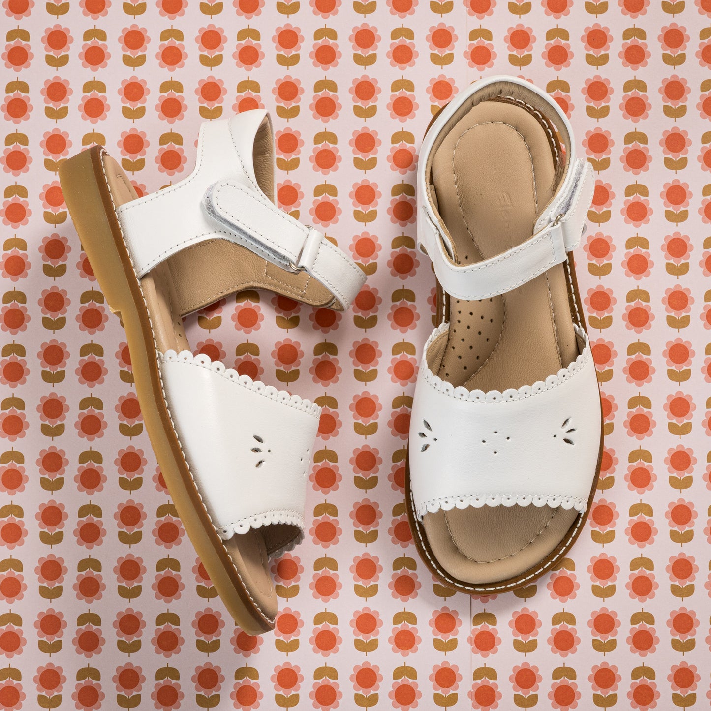 White toddler sandal with scalloped edges and perforated flower design on tan sole.