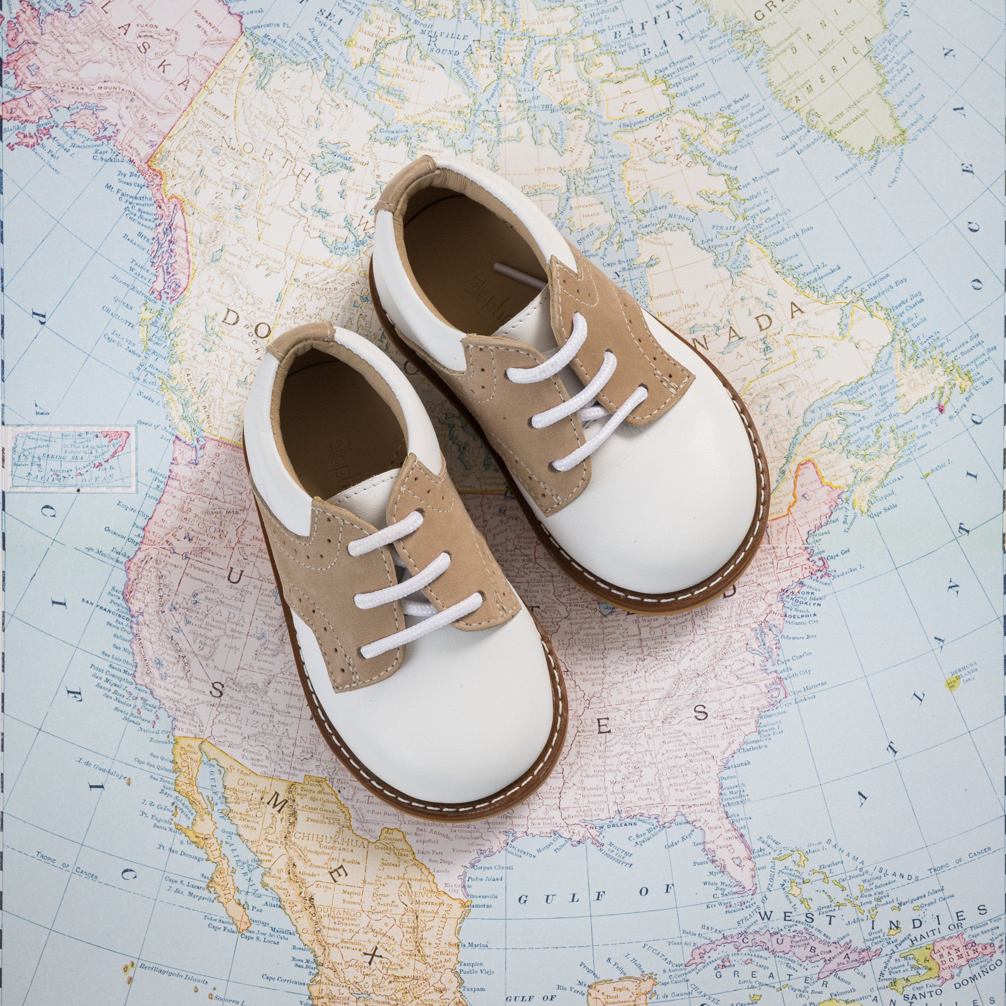 Toddlers' white and ivory slip-on shoes with laces and textured side panels on a map background.