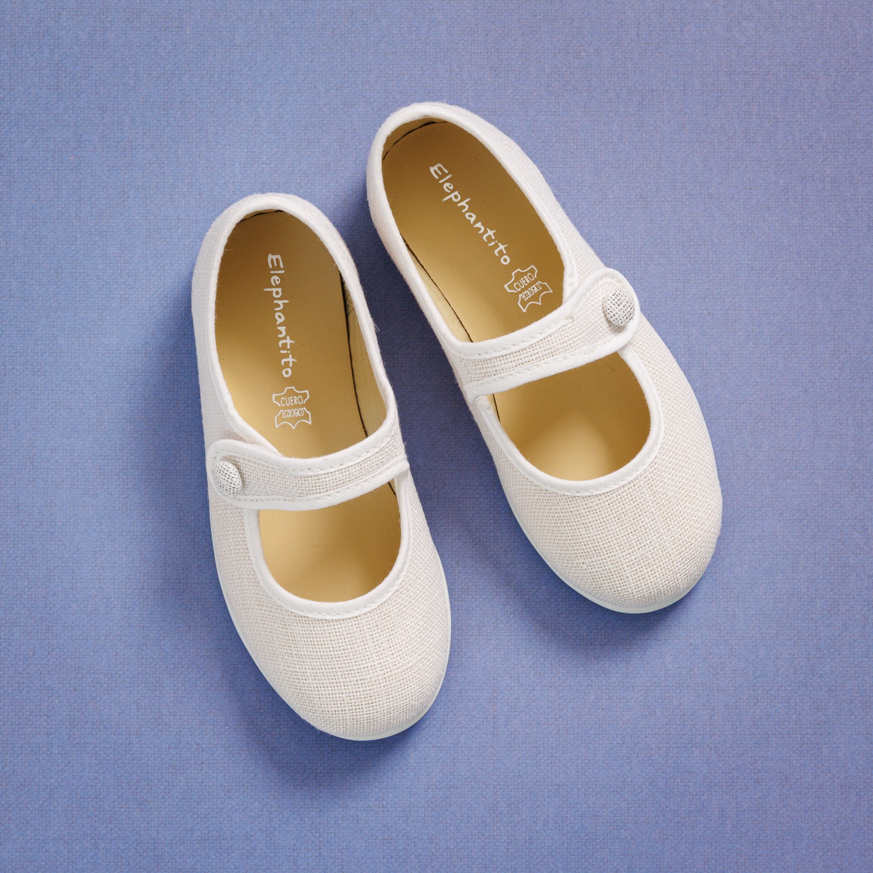 Elephantito - White linen Mary Jane shoes for girls with buttoned straps and rounded toes on blue background.