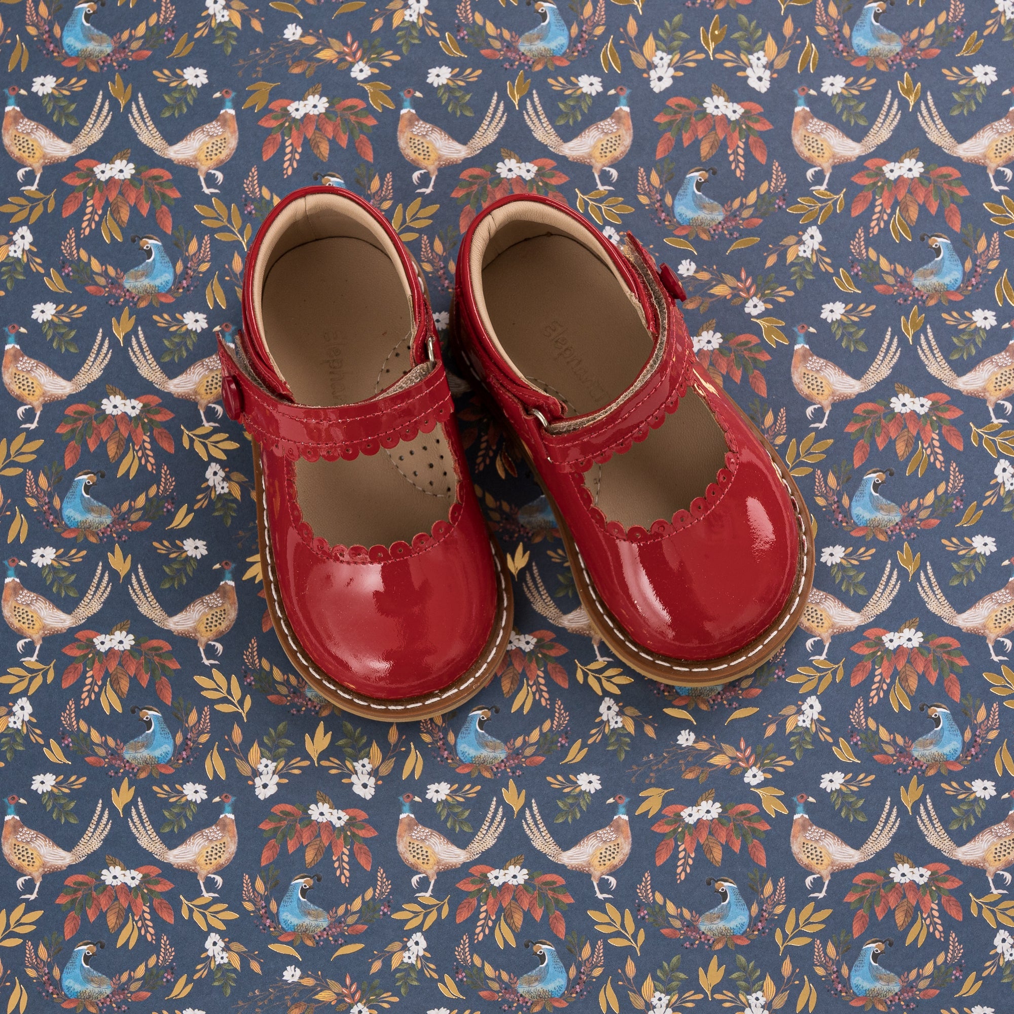 Red patent leather toddler Mary Jane shoes with buckle straps and beige soles.