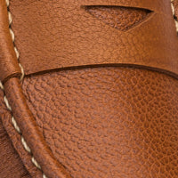 Close-up of tan pebbled leather loafer with white contrast stitching and penny slot detail.