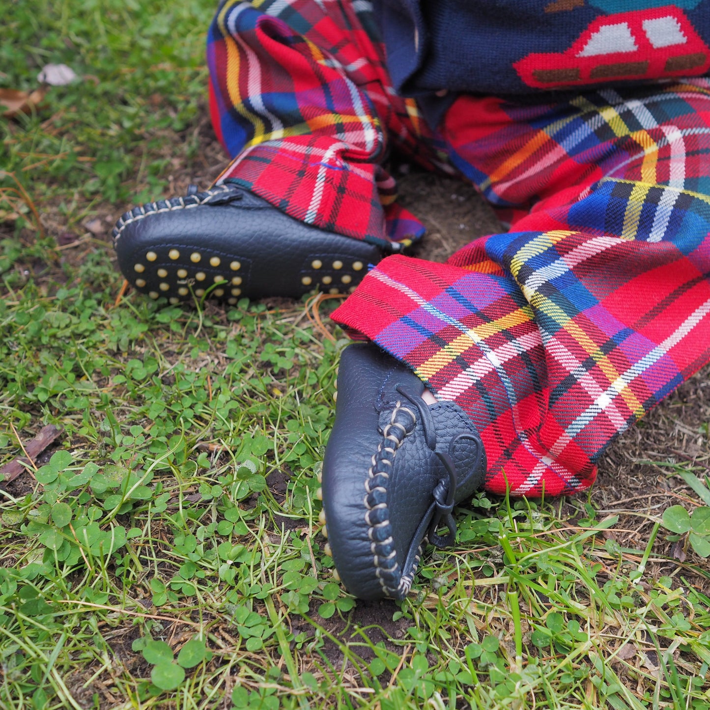 Navy blue baby driver loafers with stitched detailing and rubber pebble soles on toddler feet in multicolored plaid pants.