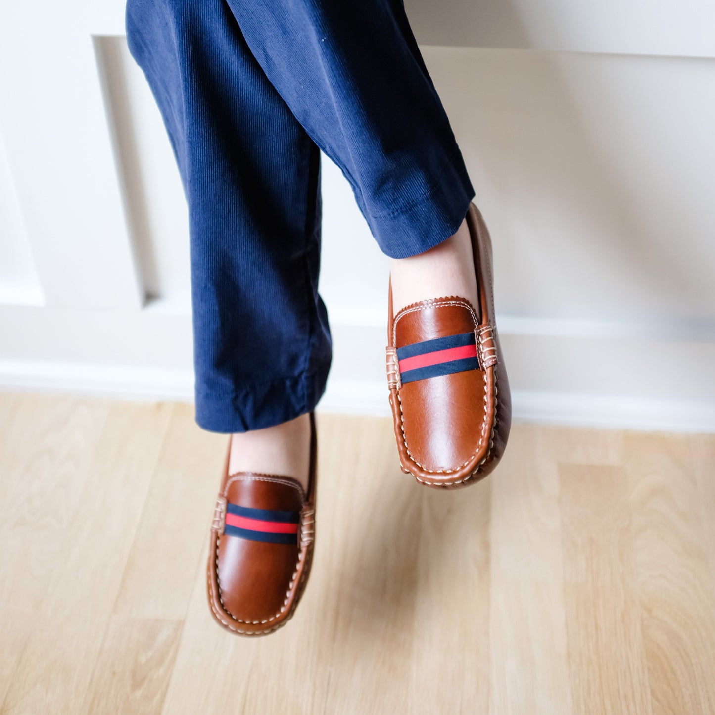 Natural brown leather baby loafers with navy and red striped fabric detail and contrast stitching.