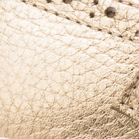 Close-up of textured metallic gold leather with stitched detailing on Mary Jane sneaker.