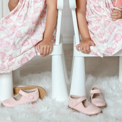 Pair of light pink Mary Jane shoes with a strap and buckle detail on white fluffy rug.