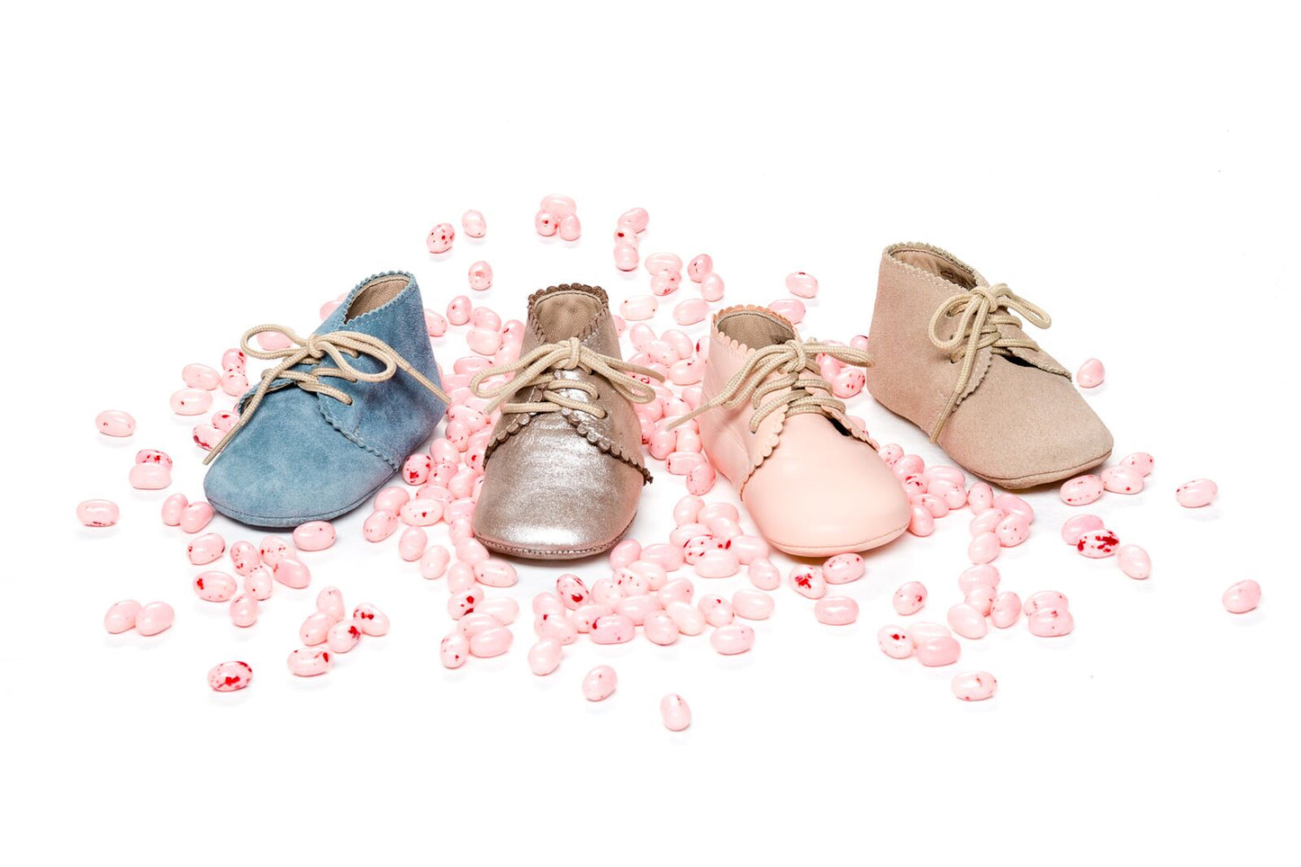 Four baby booties in blue, metallic gold, pale pink, and beige, surrounded by pink flower petals.