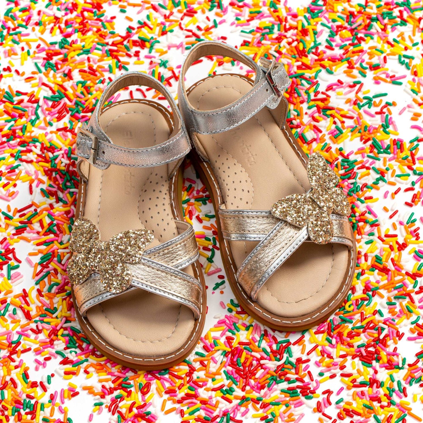Toddler girl’s gold glitter crossed strap sandals with butterfly embellishment and adjustable ankle buckle.
