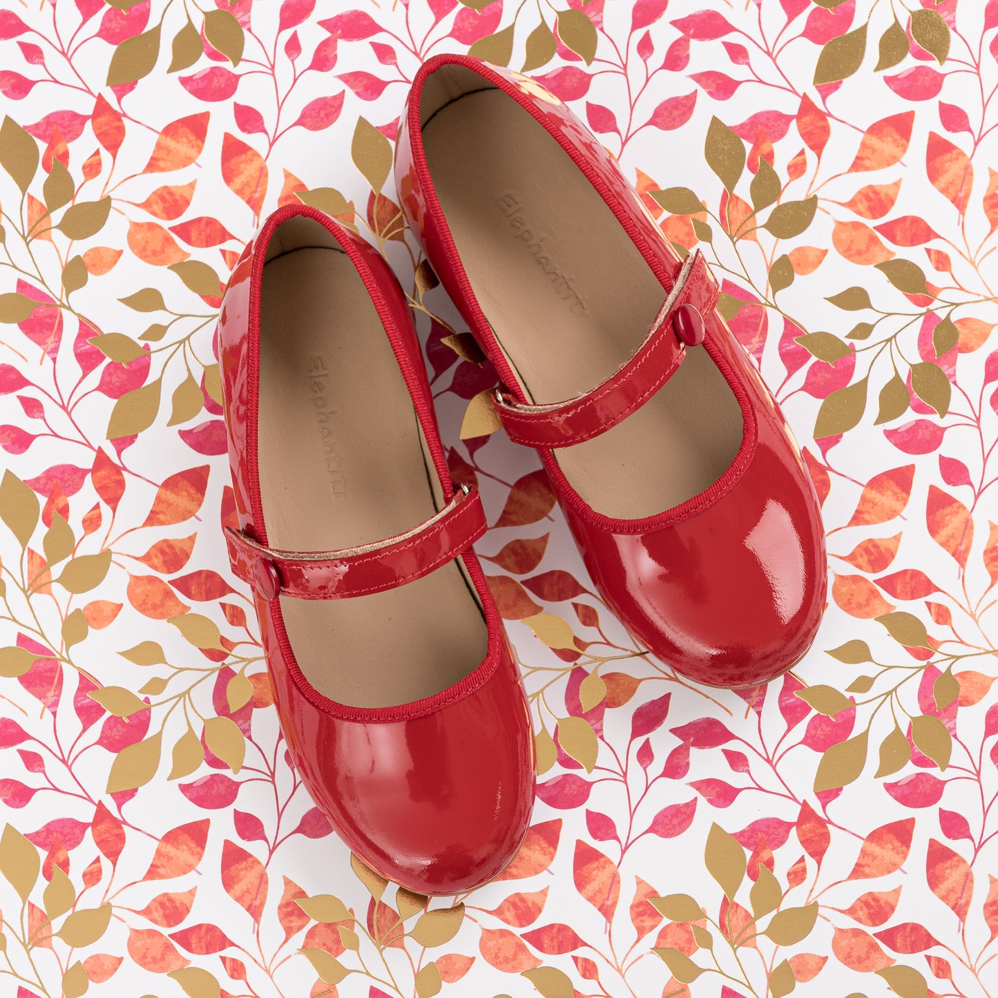 Glossy patent red Mary Jane flats with rounded toes and adjustable straps for toddlers.
