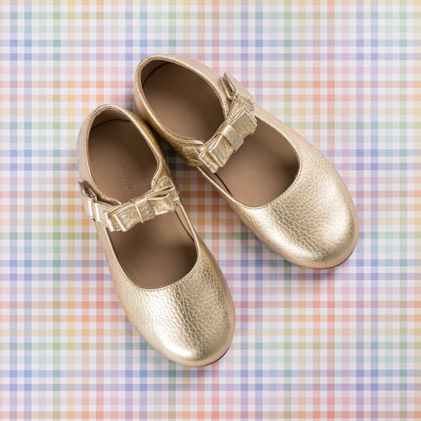 Gold metallic leather girls Mary Jane shoes with buckle straps on pastel plaid background.