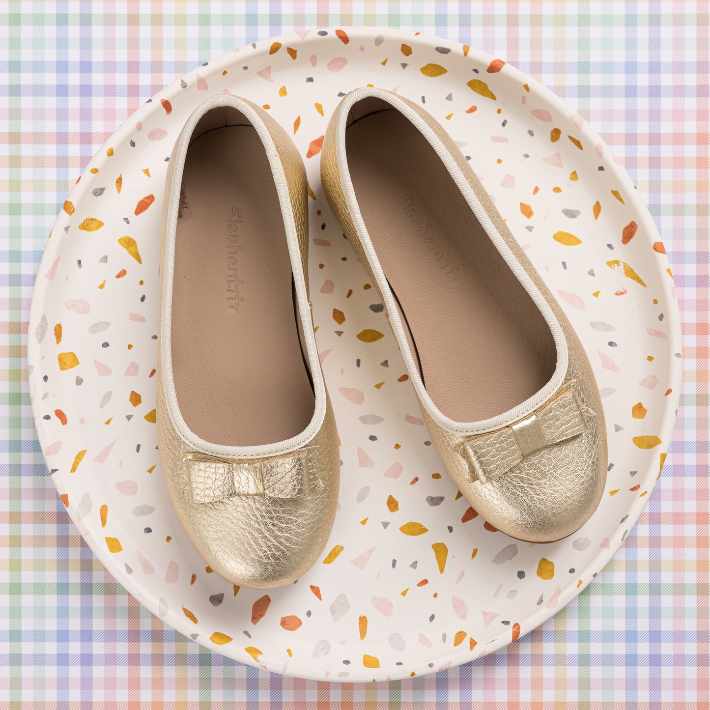 Gold leather toddler ballerina flats with small bow detail on round toe, displayed on a terrazzo-patterned plate.