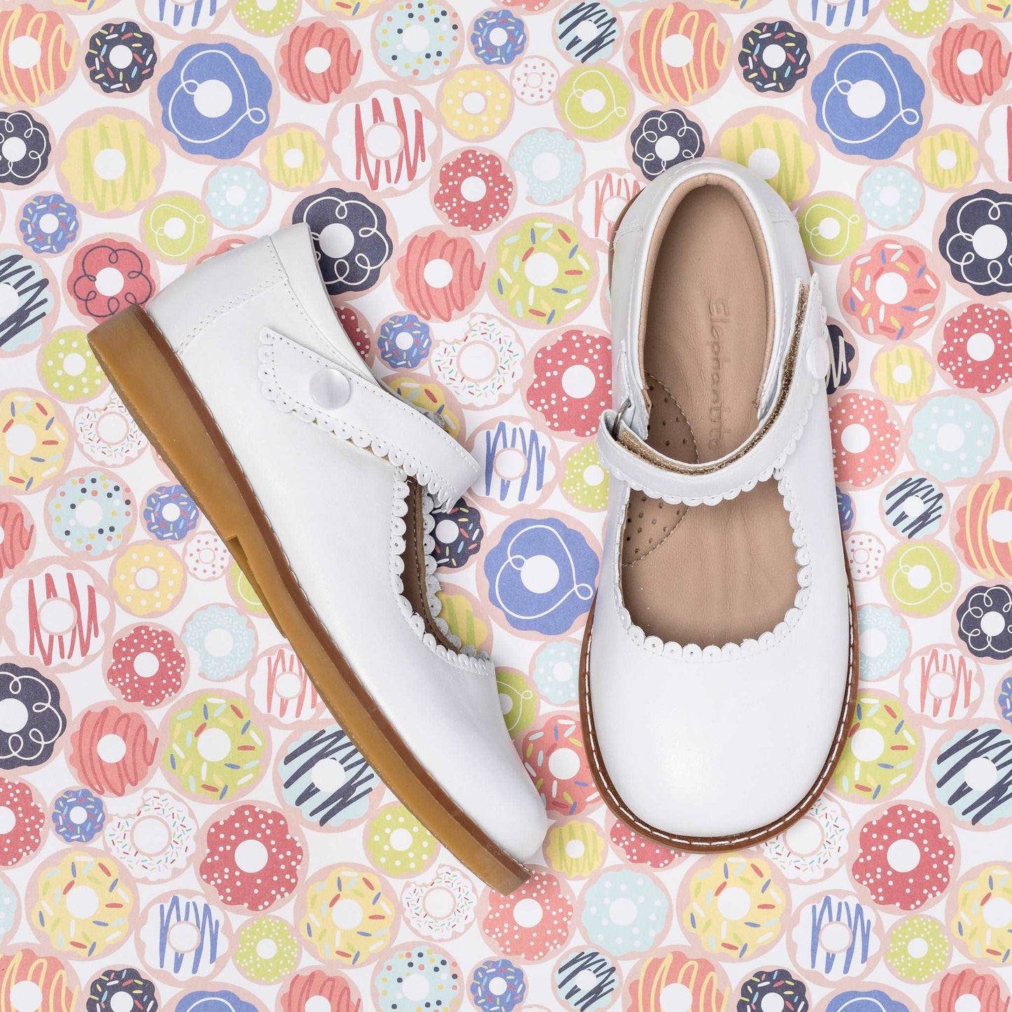 White leather Mary Jane shoes for girls with scalloped edges and a brown sole.