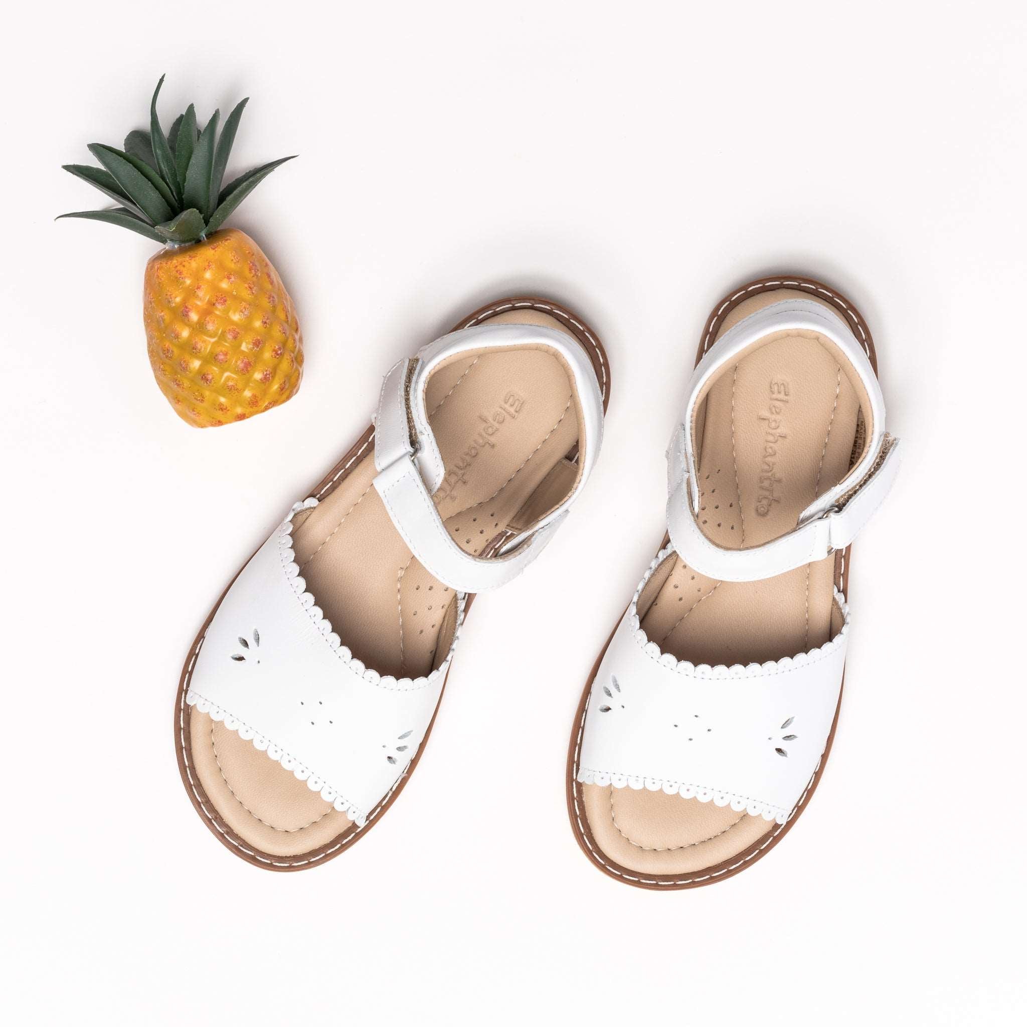 White toddler sandals with scalloped edges and perforated floral design, adjustable ankle straps.