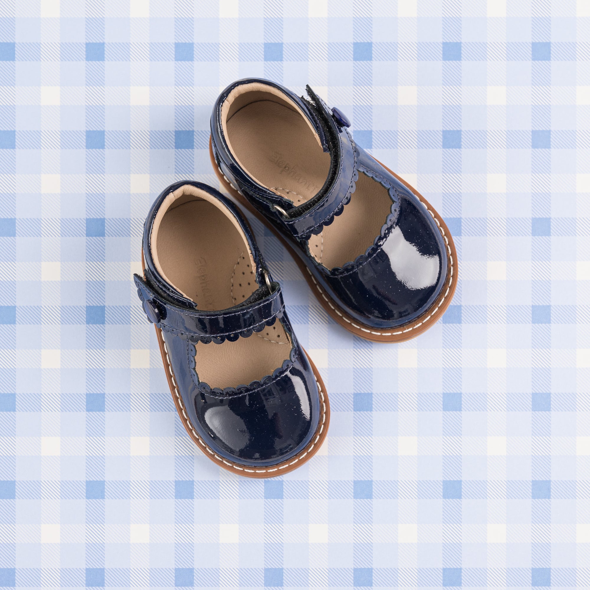 Navy blue toddler Mary Jane shoes with patent leather and scalloped edges on checkered background.