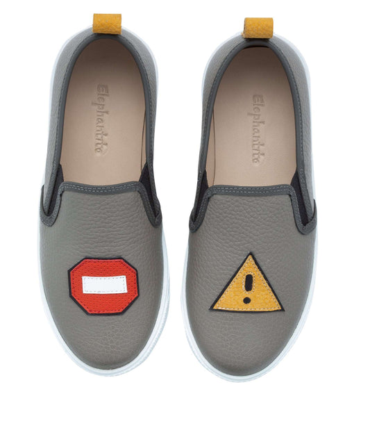 Grey slip-on kids sneakers with red stop sign on left shoe and yellow warning triangle on right shoe.