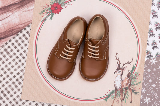Brown leather toddler shoes with white laces and rounded toes on decorative placemat.