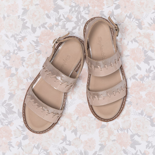 Blush pink girls' leather sandals with braided straps and ankle buckle closure on floral background.