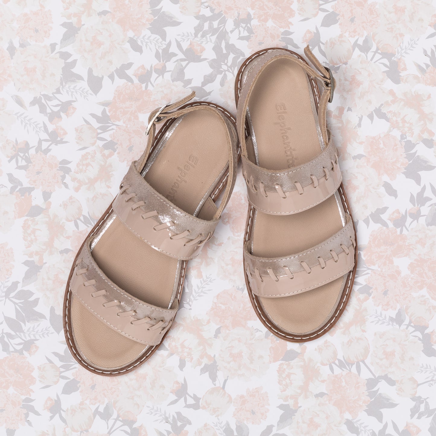 Blush pink girls' leather sandals with braided straps and ankle buckle closure on floral background.