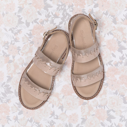 Blush pink girls' leather sandals with braided straps and ankle buckle closure on floral background.