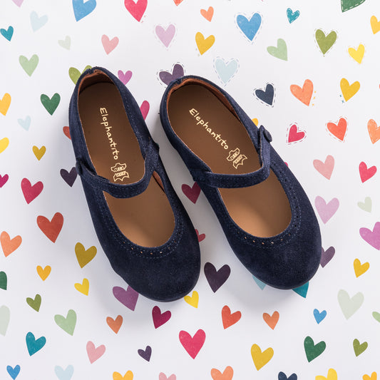 Navy blue suede Mary Jane shoes for toddlers with stitched detailing and a velcro strap on a heart-patterned background.