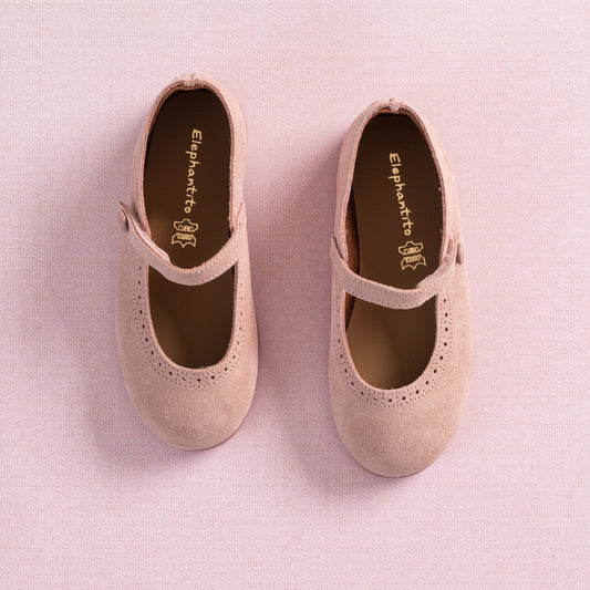 Pink suede Mary Jane shoes for toddlers with perforated detailing and buckle straps on a matching pink background.
