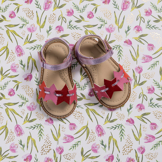 Toddler sandals with pink and fuchsia star-shaped straps and beige soles on floral background.