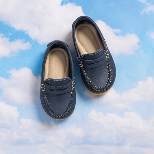 Blue toddler moccasins with stitched detailing and cushioned beige insoles on a sky background.