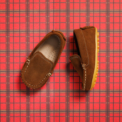 Chestnut suede toddler moccasin driver shoes with contrast yellow stitching and rubber sole on red plaid background.