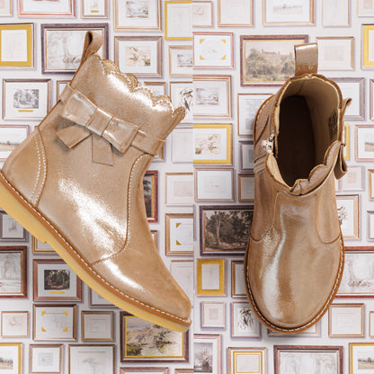 Shiny blush pink toddler booties with scalloped edges and decorative bow on side.