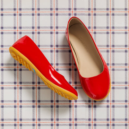 Shiny red toddler ballerina flats with tan cushioned insoles and flexible yellow rubber soles on plaid background.