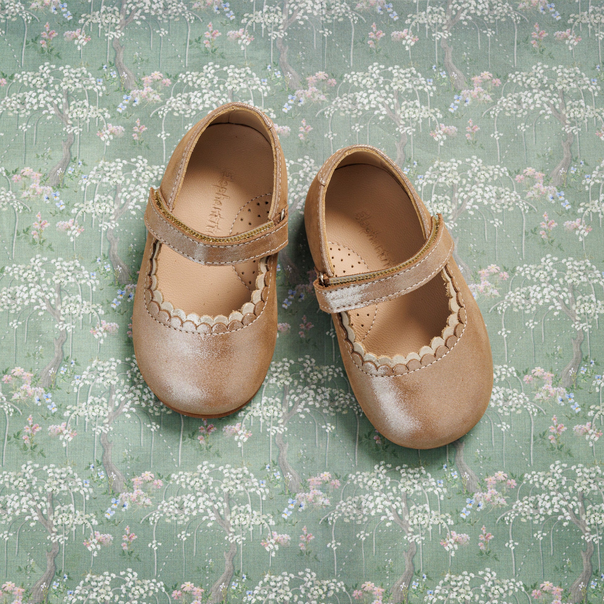 Blush pink toddler Mary Jane shoes with scalloped edges and Velcro straps on floral background.