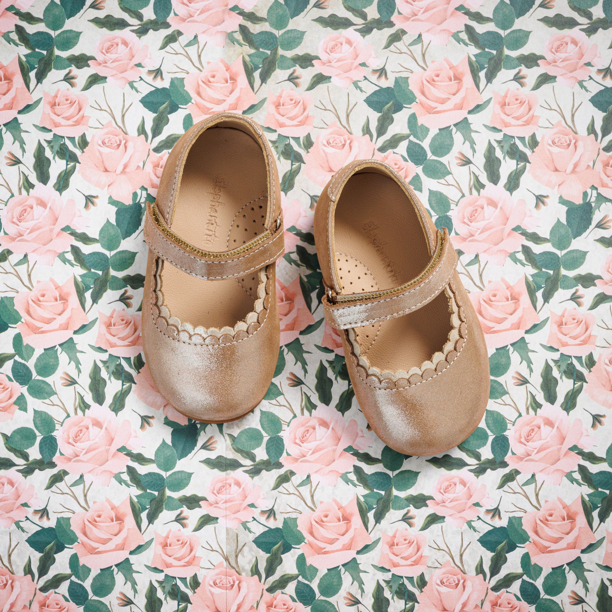 Blush pink toddler Mary Jane shoes with scalloped edges and a velcro strap on floral background.