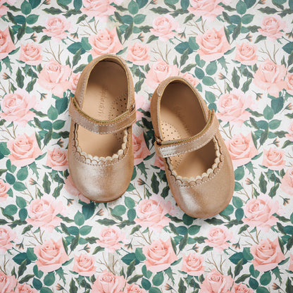 Blush pink toddler Mary Jane shoes with scalloped edges and a velcro strap on floral background.