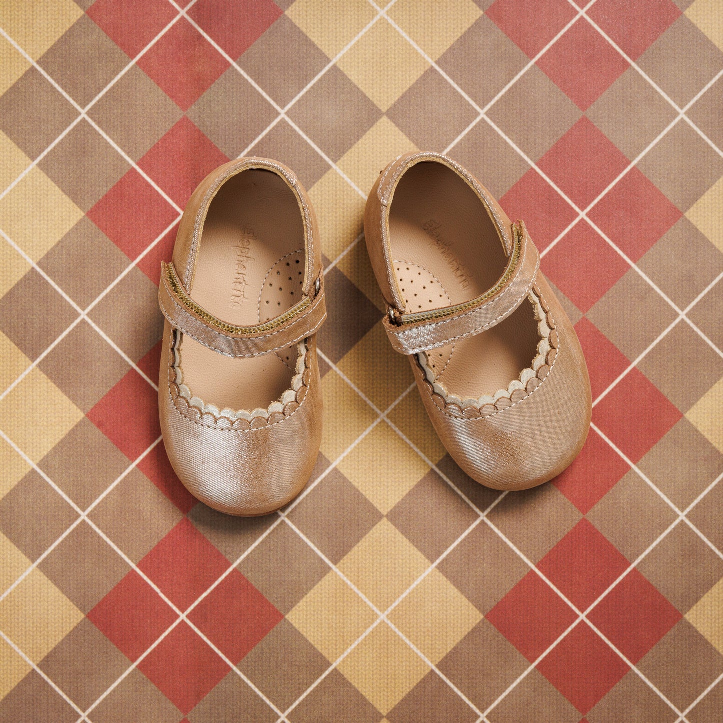 Blush pink toddler Mary Jane shoes with scalloped edge and velcro strap on plaid background.