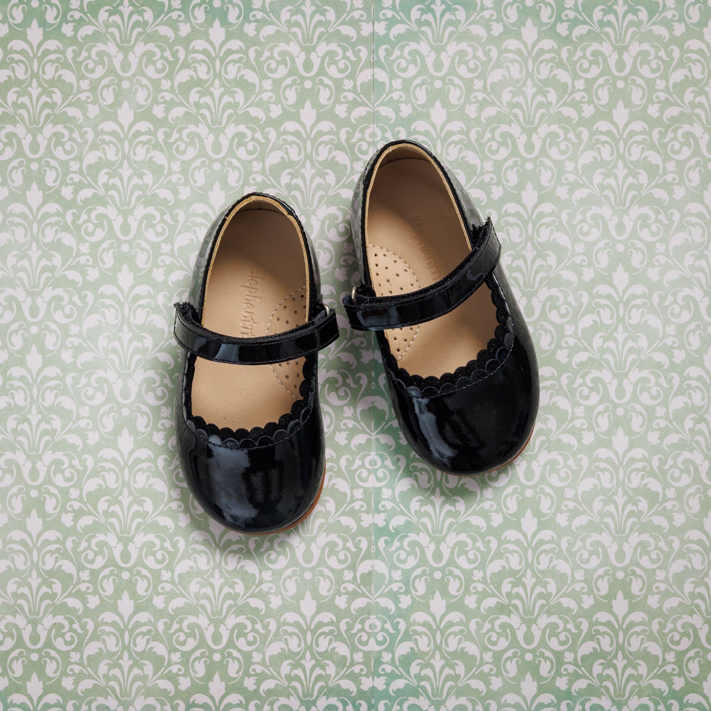 Black patent leather toddler Mary Jane flats with scalloped edges and single strap closures.