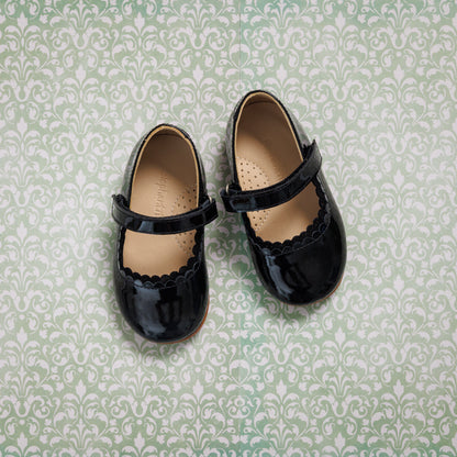 Black patent leather toddler Mary Jane flats with scalloped edges and single strap closures.