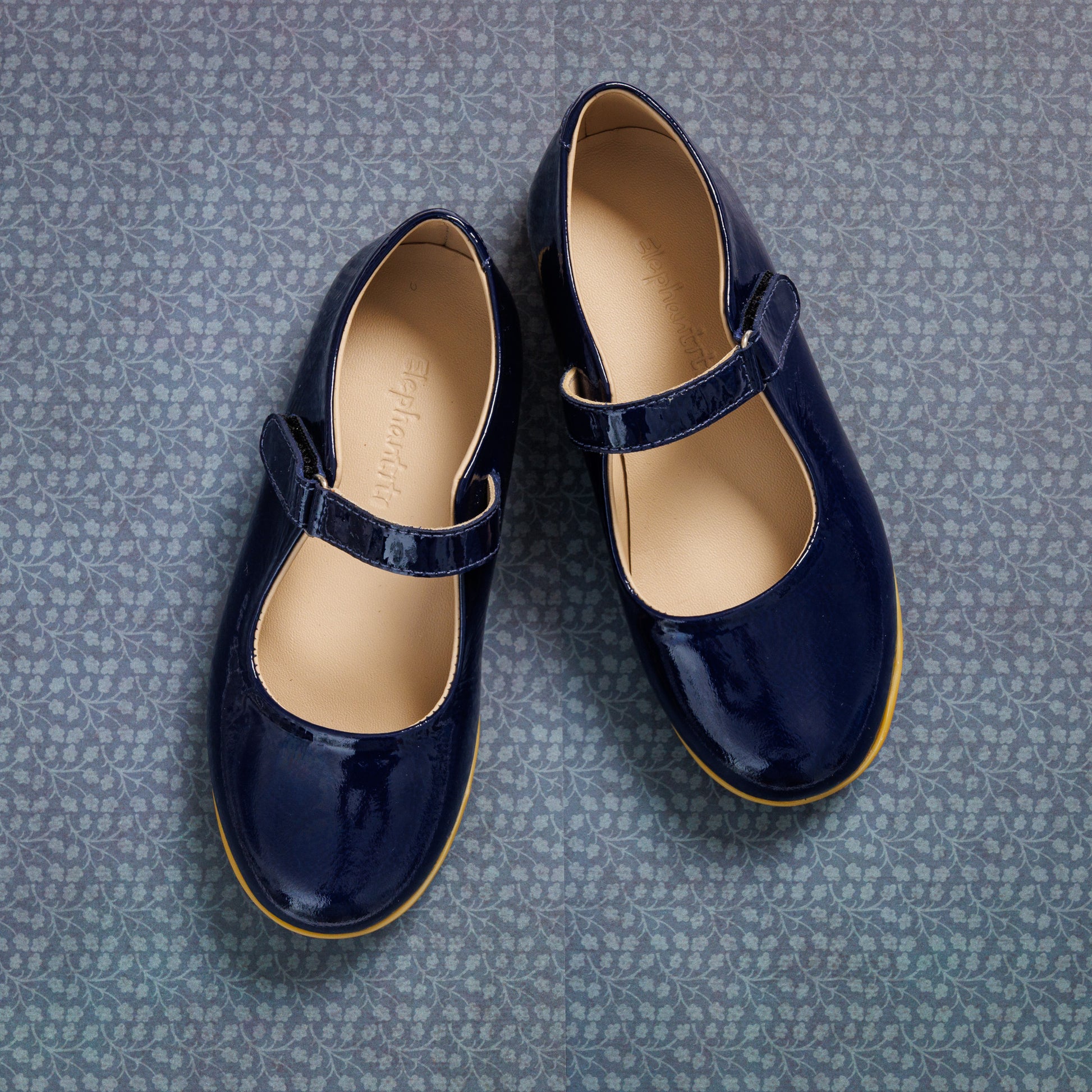 Glossy navy blue patent leather girls Mary Jane shoes with single Velcro strap and tan sole lining.