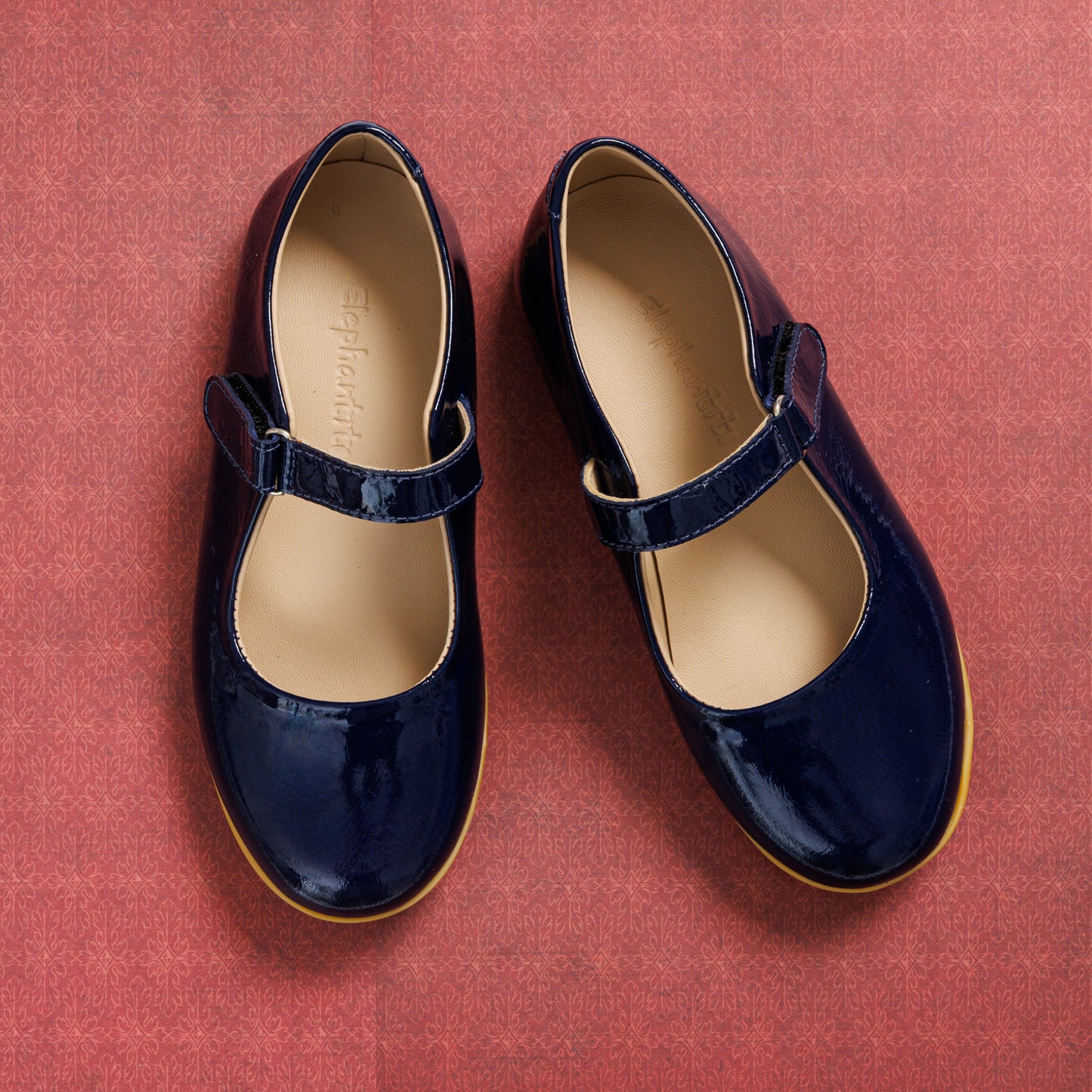 Navy blue patent leather Mary Jane shoes with Velcro strap and tan rubber sole for girls.