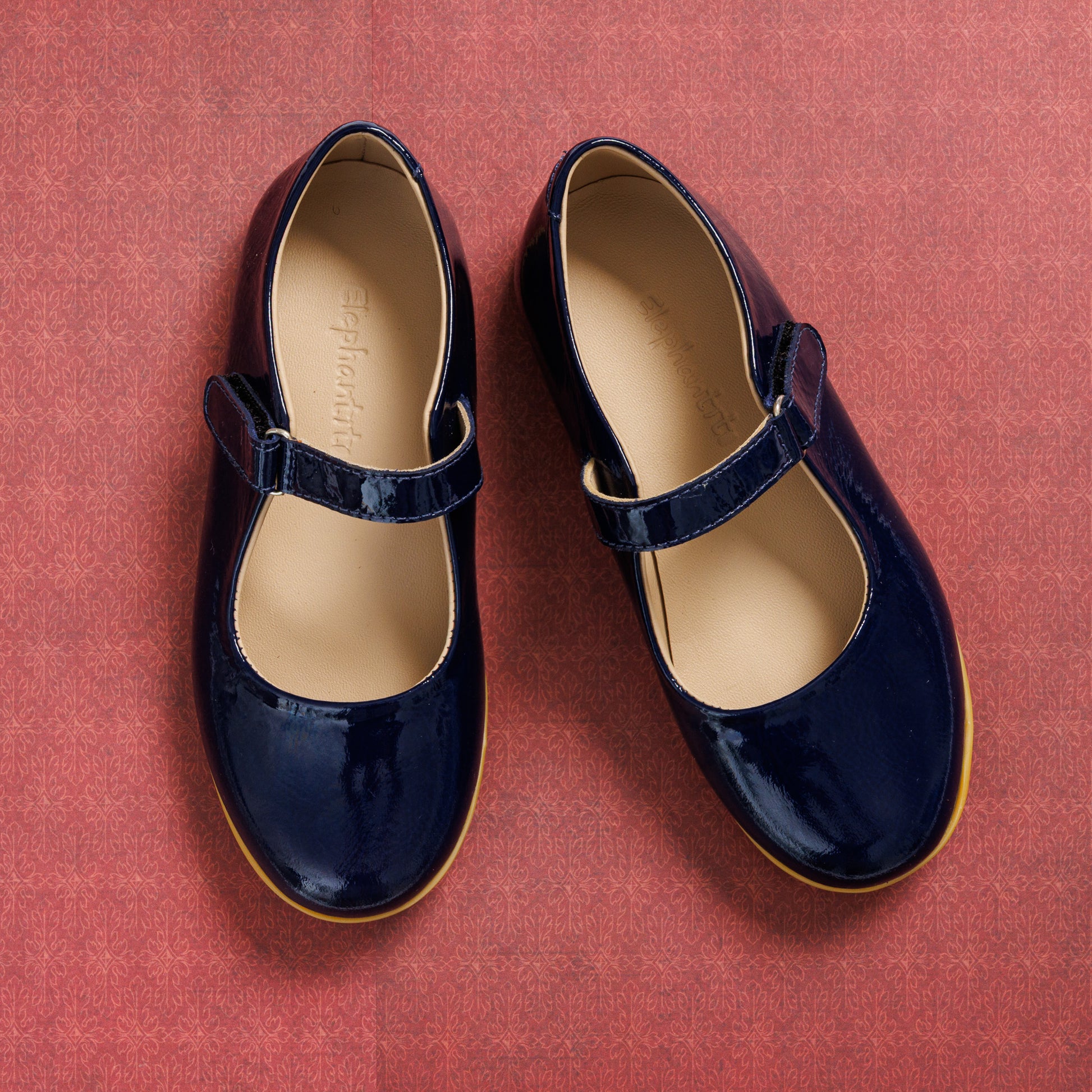 Navy blue patent leather Mary Jane shoes with Velcro strap and tan rubber sole for girls.