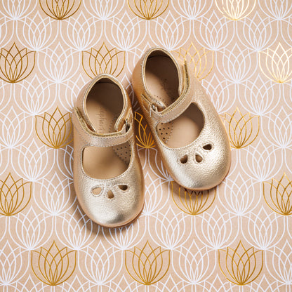 Gold toddler Mary Jane shoes with cutout heart details and Velcro strap closures on patterned background.