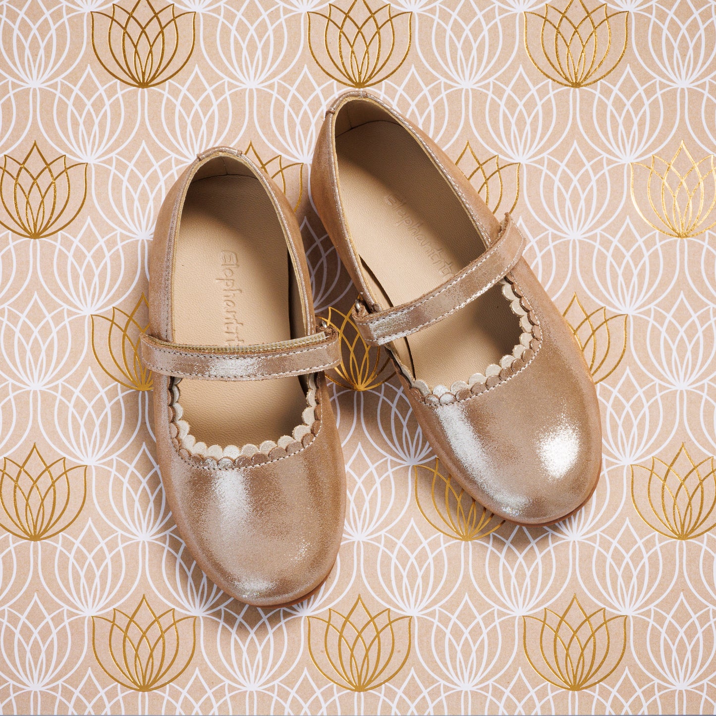 Shiny blush pink toddler Mary Jane flats with scalloped trim and single strap on patterned background.