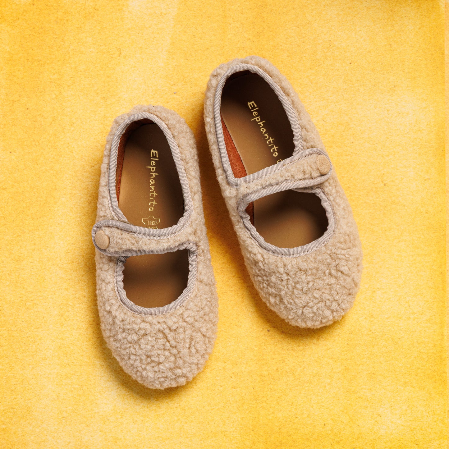 Beige shearling Mary Jane toddler shoes with rounded toe and single strap closure on yellow background.