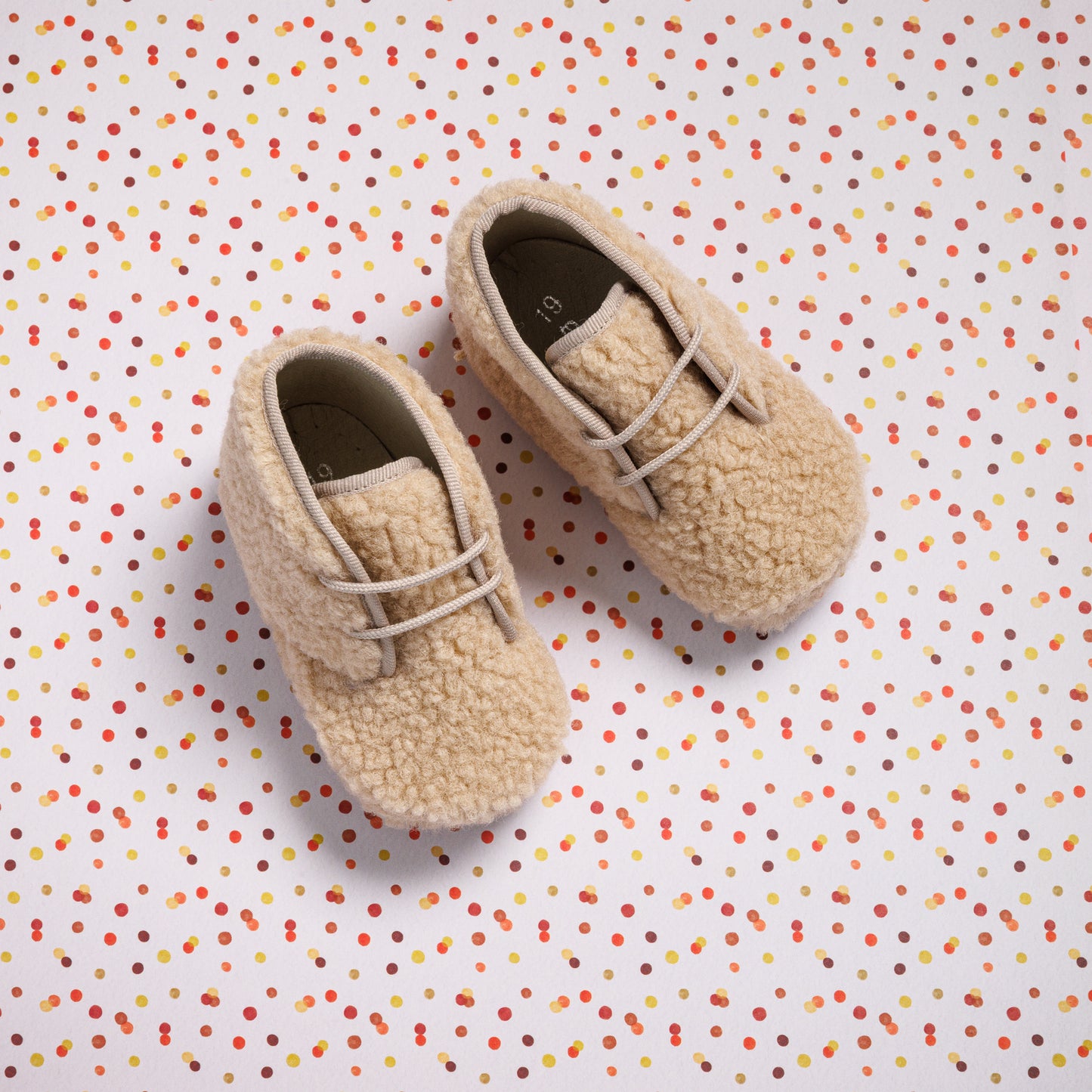 Beige shearling baby booties with lace-up front and soft textured exterior.