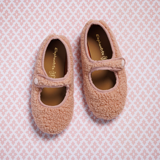 Pink toddler Mary Jane shoes with soft shearling texture and Velcro strap on pink patterned background.