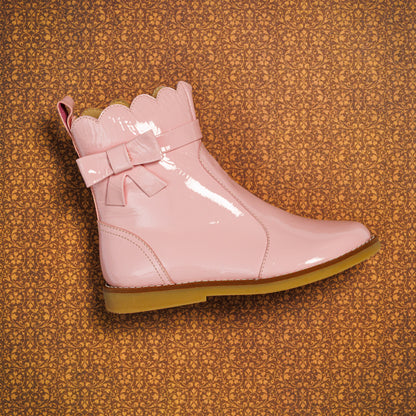 Glossy light pink toddler bootie with scalloped top edge, decorative bow, and tan sole.