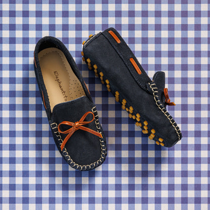 Elephantito - Navy blue suede boys' driver loafers with orange bow and rubber pebble sole detailing on gingham background.