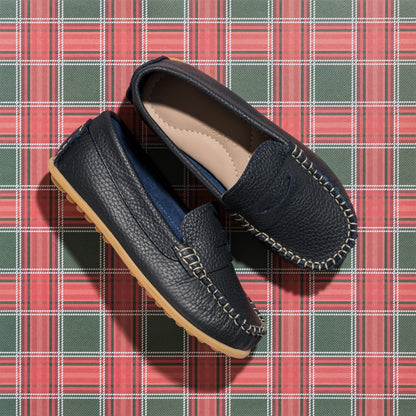Navy blue leather boys loafers with tan stitching and rubber sole on red plaid background.