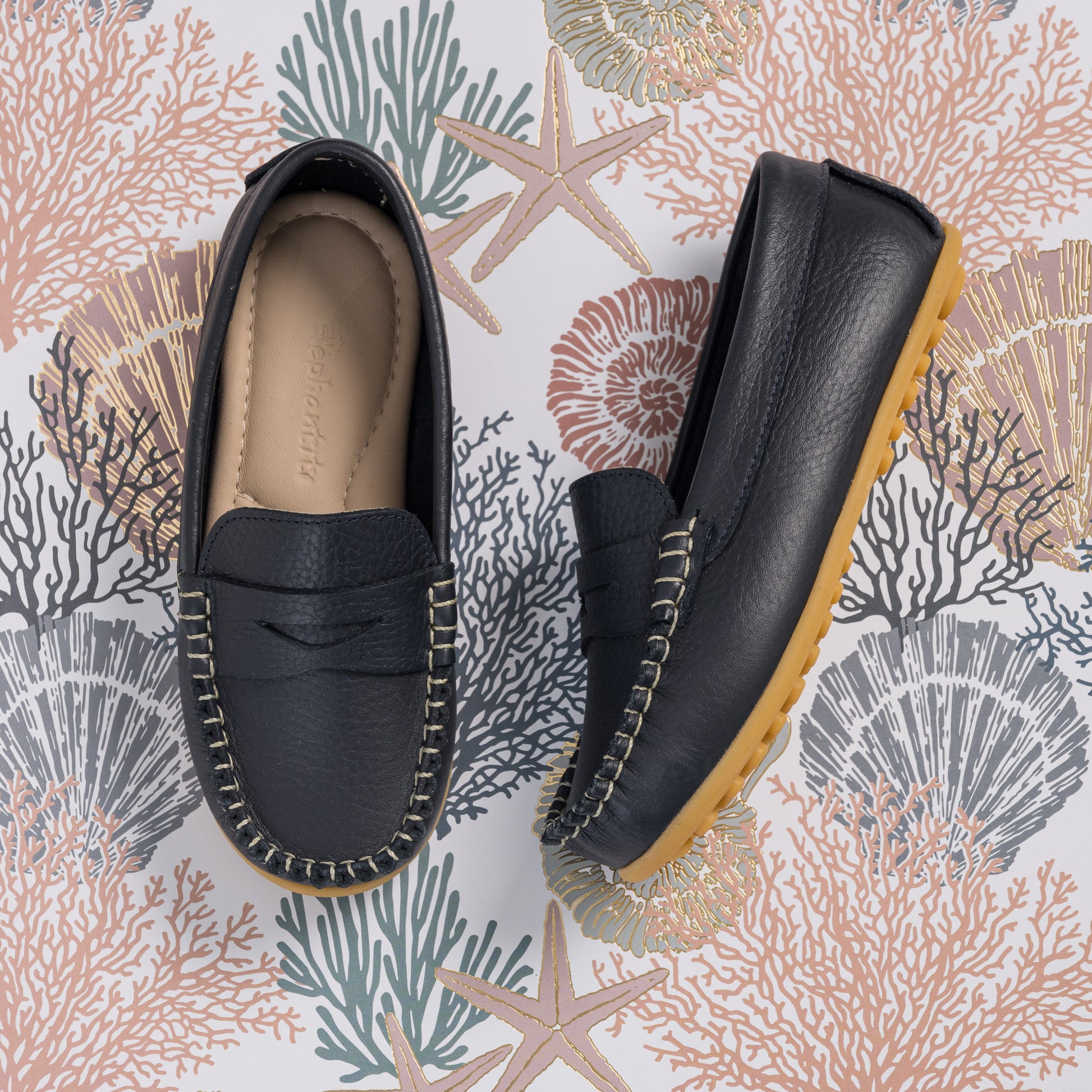 Navy blue leather boys loafers with moccasin stitching and a tan rubber sole.