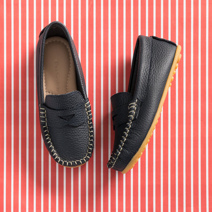 Navy blue toddler leather loafers with moccasin stitching and tan rubber soles on red striped background.